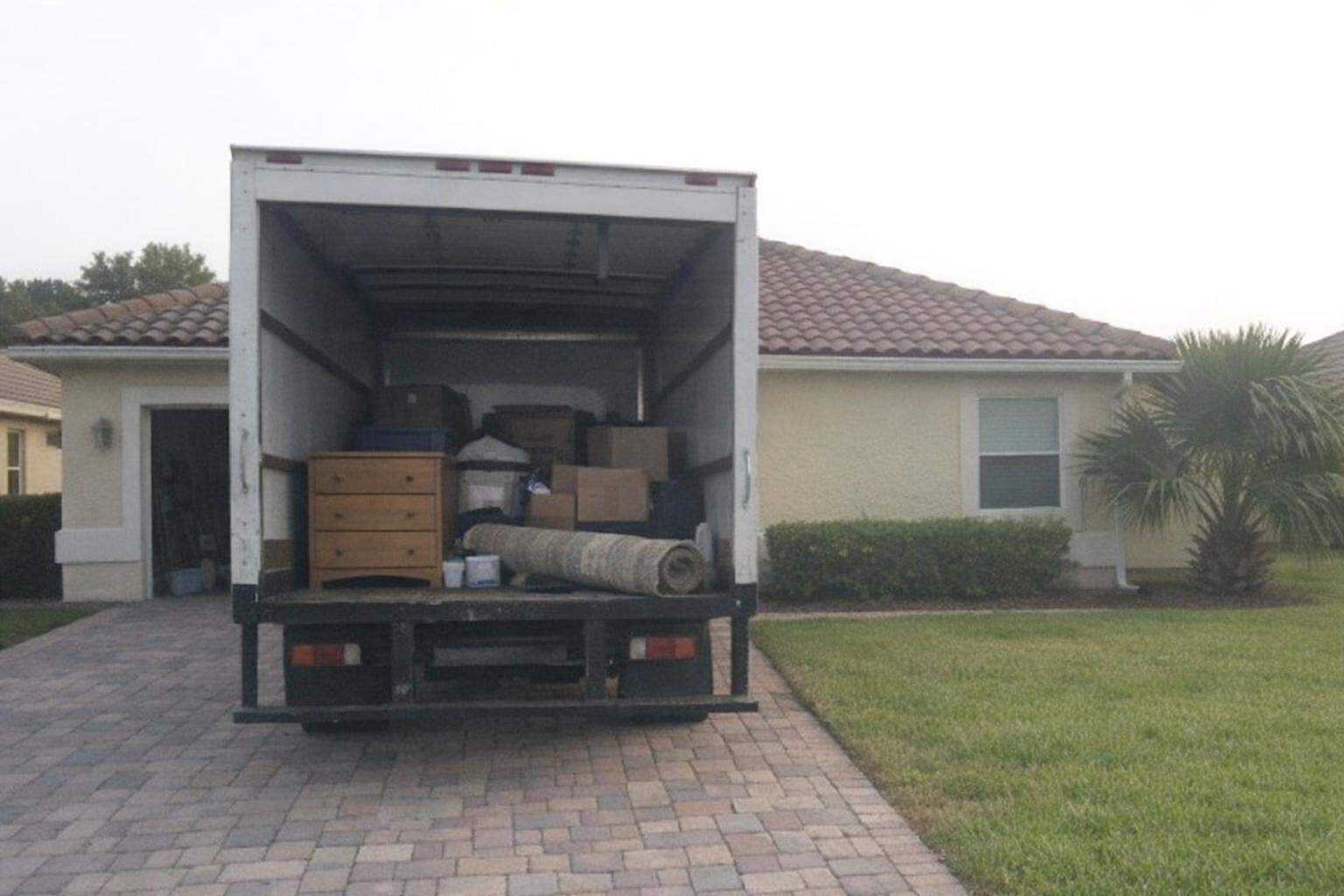 A white box truck with its rear door open, half loaded, backed onto the paver driveway of a stucco house in Orlando