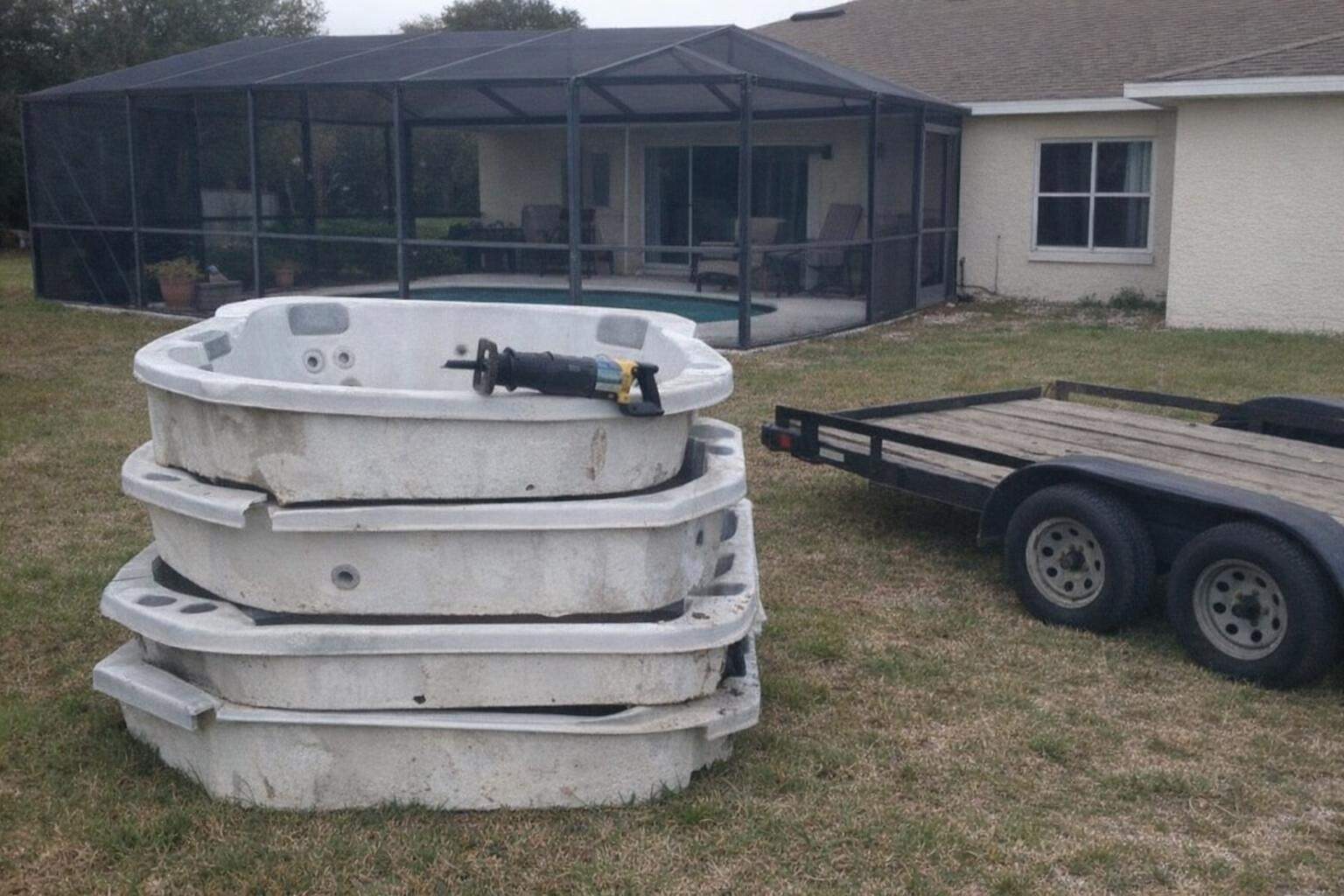 An empty hot tub shell cut into four sections stacked on a lawn next to a flatbed trailer