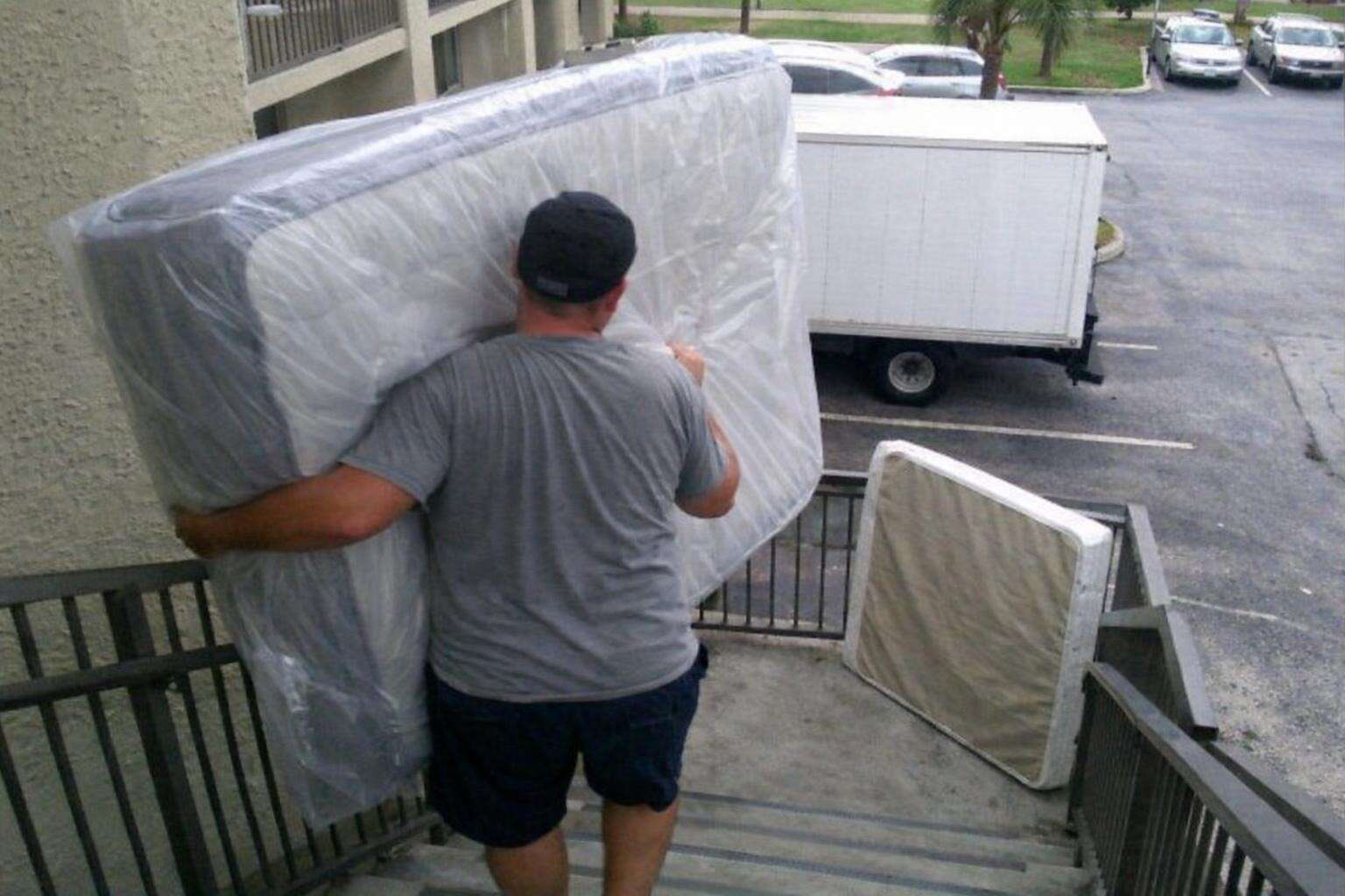A bagged queen mattress being carried down the exterior stairwell of an Orlando apartment building
